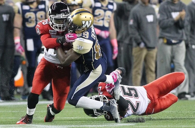 Clarence Denmark #89 of the Winnipeg Blue Bombers is taken down by Brandon Smith #28 and Keon Raymond #25 of the Calgary Stampeders in second half action in a CFL game at Investors Group Field on October 18, 2014 in Winnipeg, Manitoba, Canada. The Blue Bombers vs Stampeders Betting is about to start.