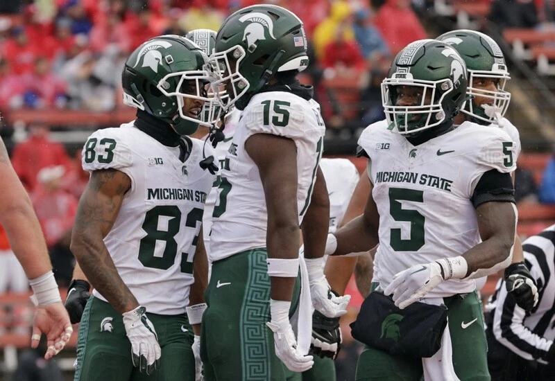 Wide receiver Montorie Foster Jr. #83 of the Michigan State Spartans celebrates his touchdown with wide receiver Jaron Glover #15 and running back Nathan Carter #5 of the Michigan State Spartans against the Rutgers Scarlet Knights. The Michigan vs Michigan State Betting Odds are set.
