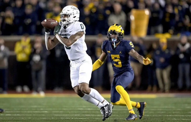 Keon Coleman #0 of the Michigan State Spartans receives a pass against DJ Turner #5 of the Michigan Wolverines. The Michigan vs Michigan State Betting Odds are set.