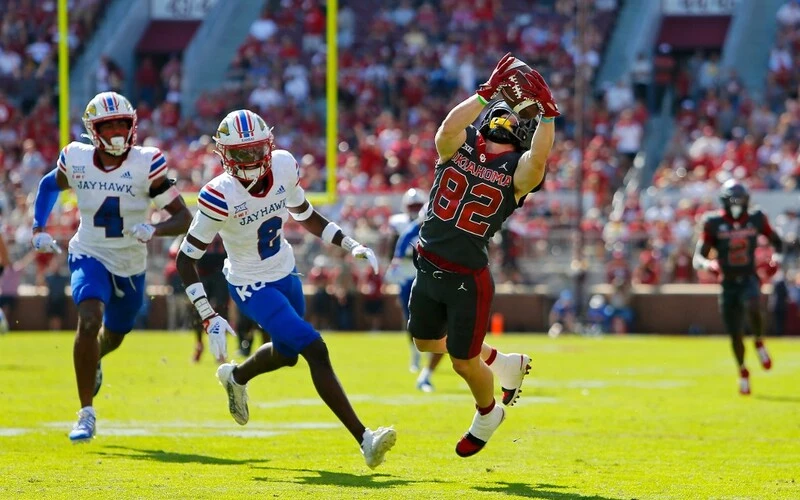 Wide receiver Gavin Freeman #82 of the Oklahoma Sooners pulls down a 41-yard catch against cornerback Cobee Bryant #2 and safety Marvin Grant #4 of the Kansas Jayhawks to set up a six yard touchdown on the next play in the second quarter at Gaylord Family Oklahoma Memorial Stadium on October 15, 2022 in Norman, Oklahoma. Oklahoma won 52-42. The Oklahoma vs Kansas Odds are set.